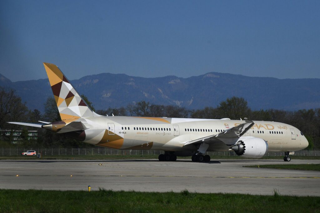 Etihad Airways plane taxiing on a runway in Genève, Switzerland under clear skies.