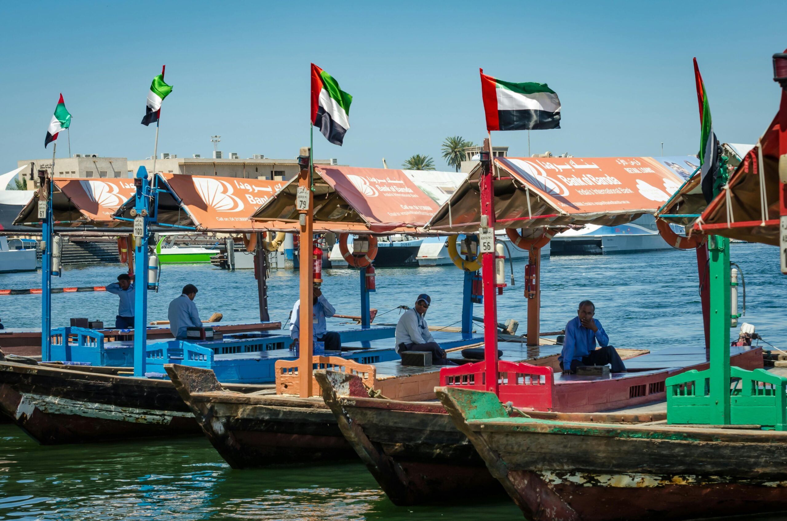 Colorful wooden boats docked with UAE flags on Dubai Creek, lively scene.